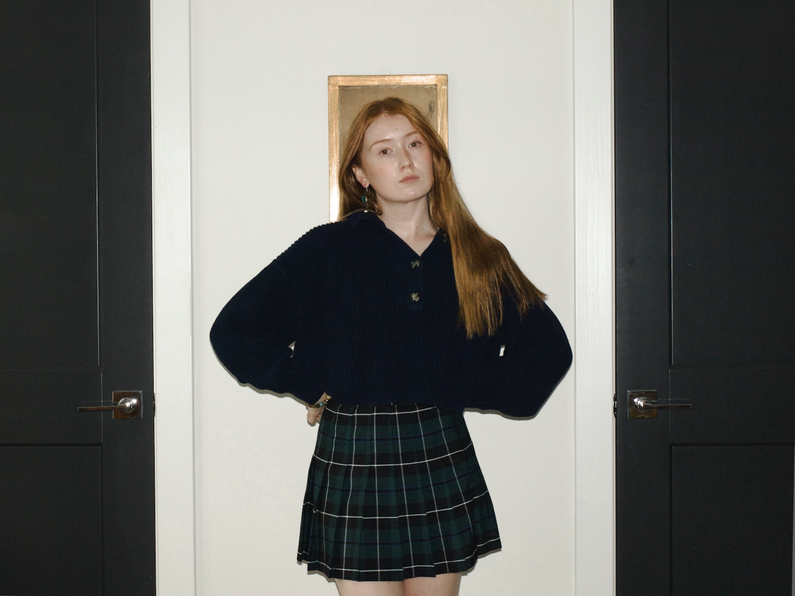 Front view of Emma wearing a navy sweater with a plaid Los Angeles Apparel tennis skirt